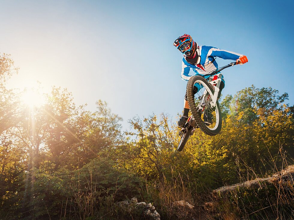 Mountainbiker springt auf einem sonnigen Offroad-Trail mit viel Airtime
