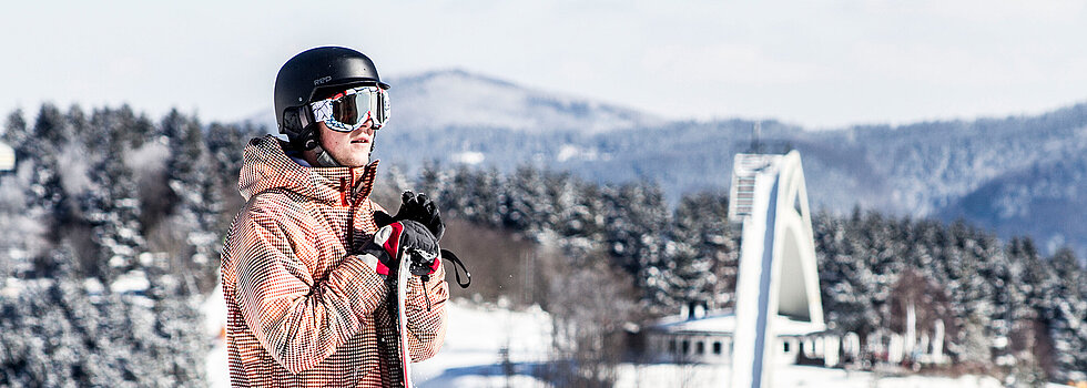 Snowboarder steht vor einer Schanze im verschneiter Winterlandschaft