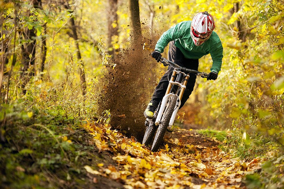 Downhill-Fahrer rast durch herbstlichen Wald und wirbelt Erde auf