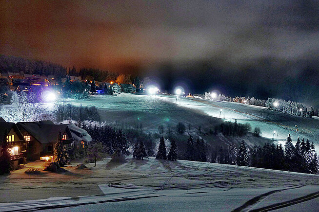 Beleuchtete Skipiste in Winterberg bei Nacht mit Flutlicht und verschneiter Landschaft