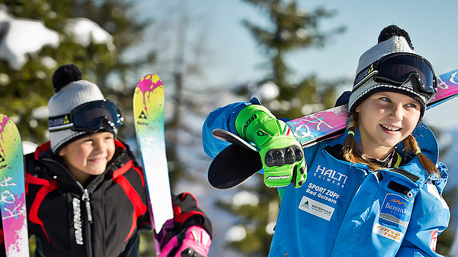 Zwei Kinder mit bunten Ski gehen durch verschneite Winterlandschaft